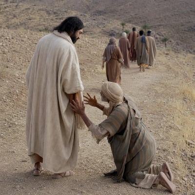 A Samaritan formerly afflicted with leprosy kneels before Jesus in gratitude as the other nine walk away on the road to the priests.