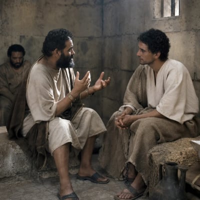 Joseph standing in an Egyptian prison beside the chief butler, who describes a vine with three branches while Joseph interprets the dream.